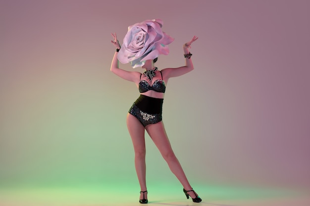 Delighted. Young female dancer with huge floral hats in neon light on gradient wall. Graceful model, woman dancing, posing. Concept of carnival, beauty, motion, blooming, spring fashion.