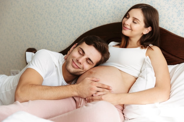 Delighted young pregnant wife lying in bed