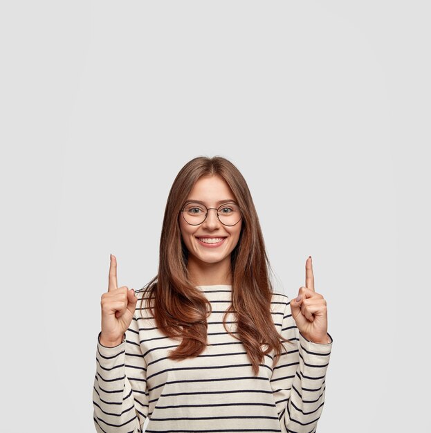 delighted young woman with glasses posing against the white wall