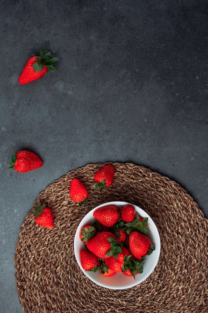 Delightful strawberries in a white bowl on a round placemat and grey grunge background. flat lay.