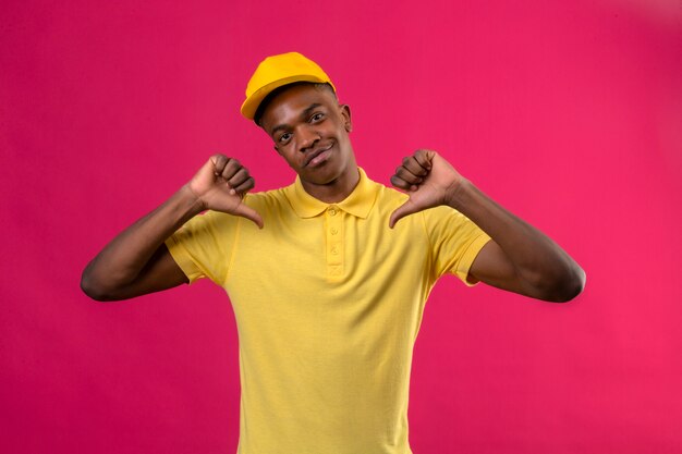 Delivery african american man in yellow polo shirt and cap looking confident pointing to himself proud self-satisfied standing on pink