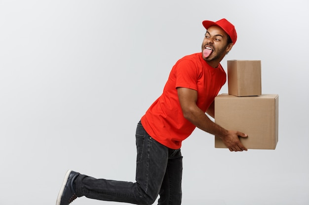 Foto gratuita concetto di consegna - bello uomo africano di consegna corsa in esecuzione per la fornitura di un pacchetto per il cliente. isolato su sfondo grigio dello studio. copia spazio.