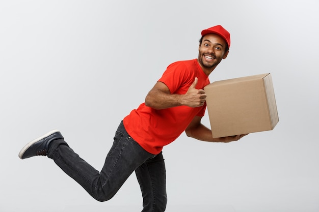 Delivery Concept - Handsome African American delivery man rush running for delivering a package for customer. Isolated on Grey studio Background. Copy Space.