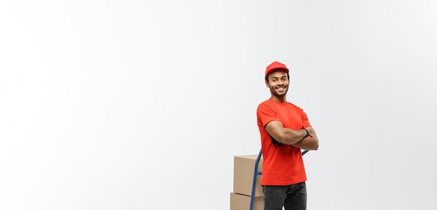 Free photo delivery concept portrait of handsome african american delivery man or courier pushing hand truck with stack of boxes isolated on grey studio background copy space