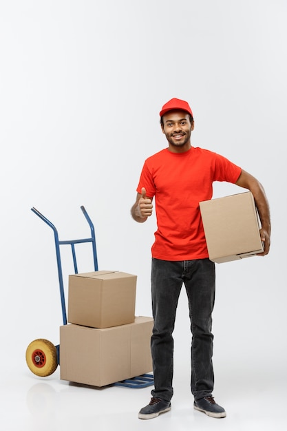 Delivery Concept - Portrait of Handsome African American delivery man or courier pushing hand truck with stack of boxes. Isolated on Grey studio Background. Copy Space.