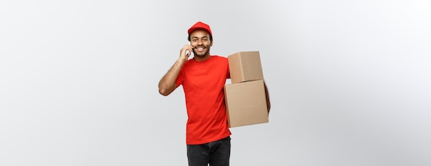 Delivery Concept Portrait of Handsome African American delivery man or courier with box calling phone to customer Isolated on Grey studio Background Copy Space