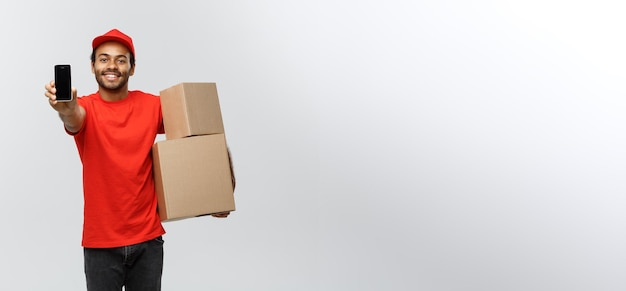 Free photo delivery concept portrait of handsome african american delivery man or courier with box showing mobile phone on you to check the order isolated on grey studio background copy space