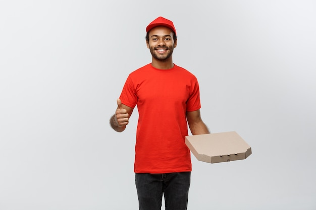 Концепция доставки - Портрет красивой афро-американской доставки пиццы человек. Изолированные на фоне серой студии. Копирование пространства.