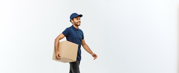 Free photo delivery concept portrait of happy african american delivery man in blue cloth walking to send a box package to customer isolated on grey studio background copy space