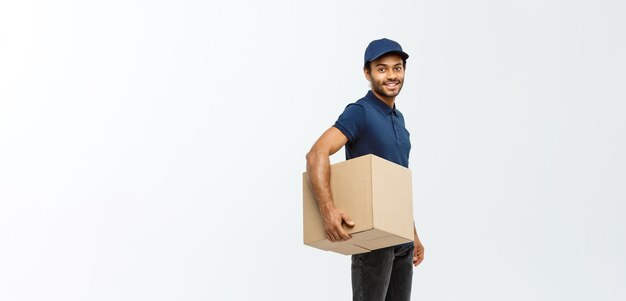 Delivery Concept Portrait of Happy African American delivery man in blue cloth walking to send a box package to customer Isolated on Grey studio Background Copy Space