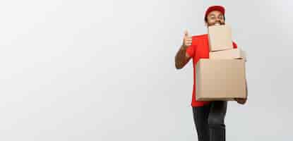 Free photo delivery concept portrait of happy african american delivery man holding box packages and showing thumps up isolated on grey studio background copy space