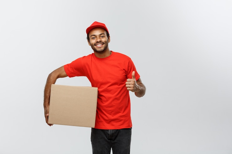 Free Photo delivery concept - portrait of happy african american delivery man holding box packages and showing thumps up. isolated on grey studio background. copy space.