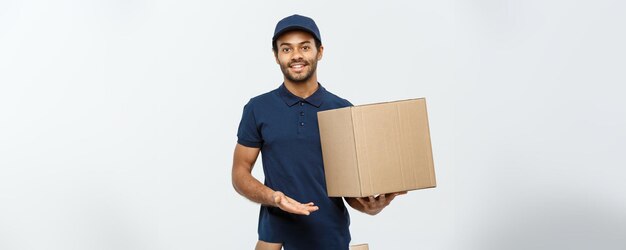 Delivery Concept Portrait of Happy African American delivery man pointing hand to present a box package Isolated on Grey studio Background Copy Space