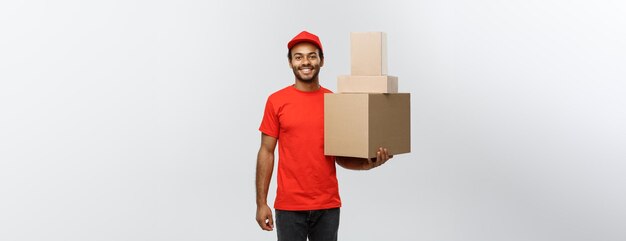 Delivery Concept Portrait of Happy African American delivery man in red cloth holding a box package Isolated on Grey studio Background Copy Space