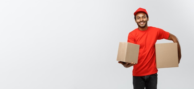 Delivery Concept Portrait of Happy African American delivery man in red cloth holding a box package Isolated on Grey studio Background Copy Space