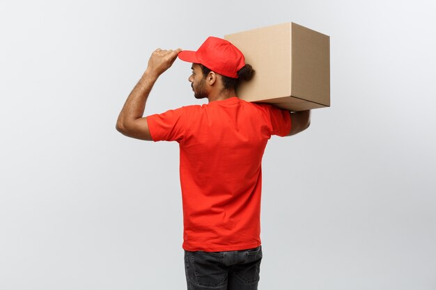 Delivery Concept - Portrait of Happy African American delivery man in red cloth holding a box package. Isolated on Grey studio Background. Copy Space.