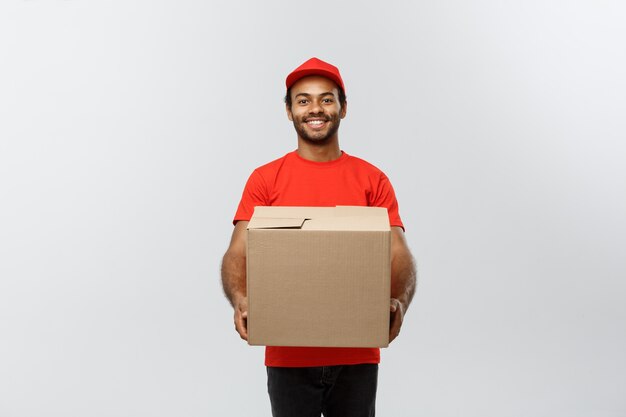 Delivery Concept - Portrait of Happy African American delivery man in red cloth holding a box package. Isolated on Grey studio Background. Copy Space.