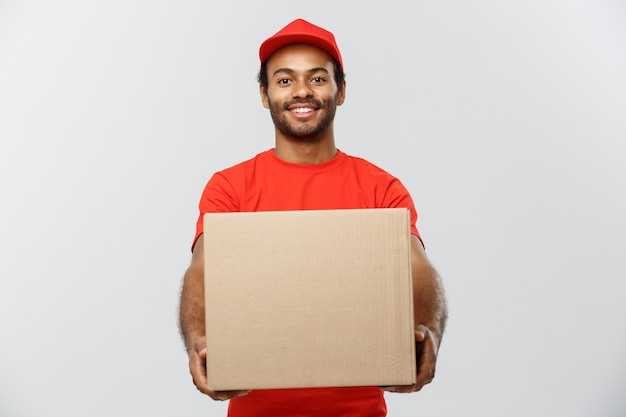 Delivery Concept - Portrait of Happy African American delivery man in red cloth holding a box package. Isolated on Grey studio Background. Copy Space.