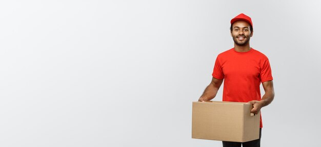Free photo delivery concept portrait of happy african american delivery man in red cloth holding a box package