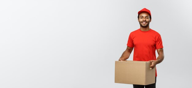 Delivery concept portrait of happy african american delivery man in red cloth holding a box package