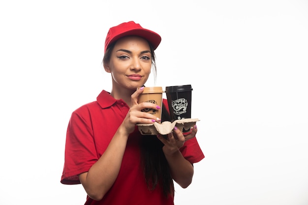 Женщина-служащий службы доставки в красной кепке держит две чашки кофе