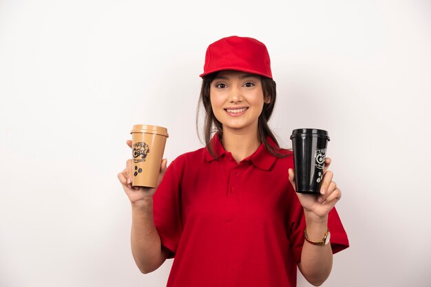 Delivery employee woman in red cap holding coffee cups on white background.