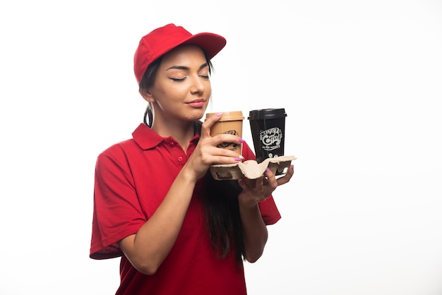 Delivery employee woman in red cap holding two cups of coffee