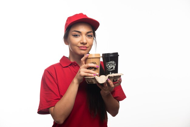 Delivery employee woman in red cap holding two cups of coffee