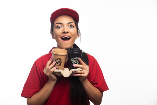 Delivery employee woman in red cap hugging two cups of coffee