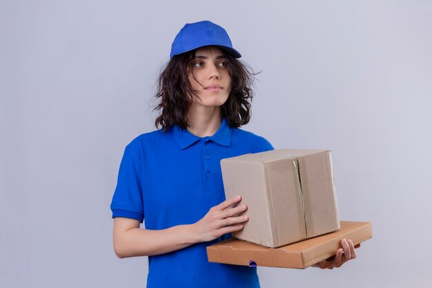 파란색 유니폼과 모자를 들고 진지하고 자신감있는 표정으로 멀리보고 상자 패키지를 들고 배달 소녀