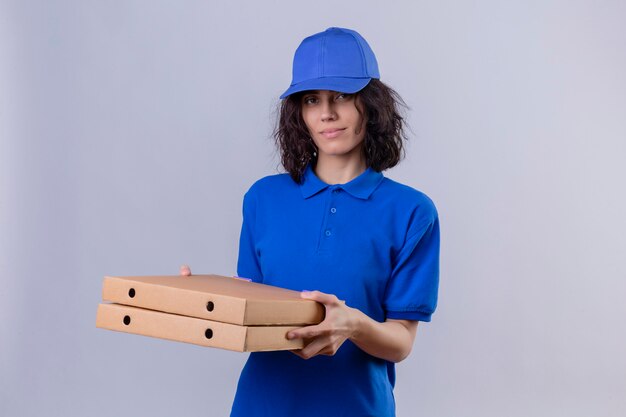 Delivery girl in blue uniform and cap holding pizza boxes smiling confident standing on white