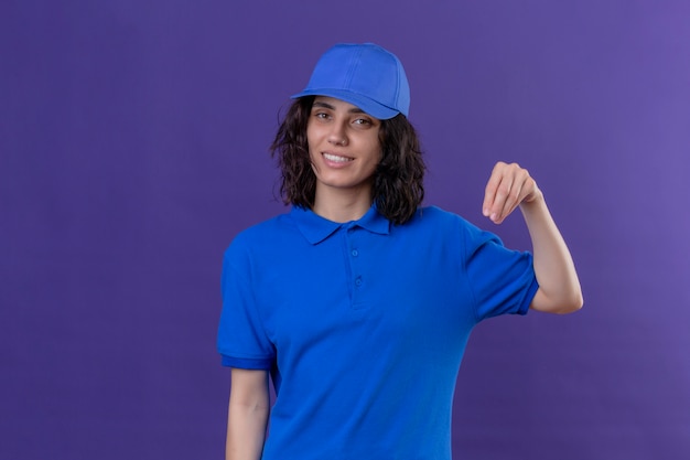 Delivery girl in blue uniform and cap looking confident gesturing with hand, body language concept standing on isolated purple