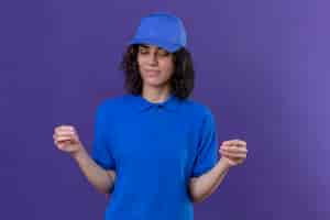 Free photo delivery girl in blue uniform and cap looking confident gesturing with hand, body language concept standing on isolated purple