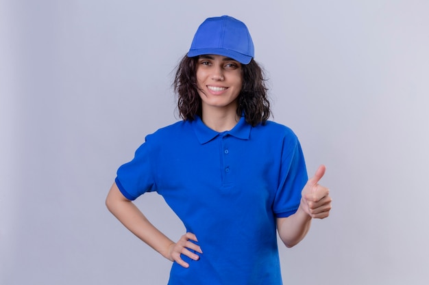 Free photo delivery girl in blue uniform and cap smiling friendly showing success , showing thumbs up standing on white