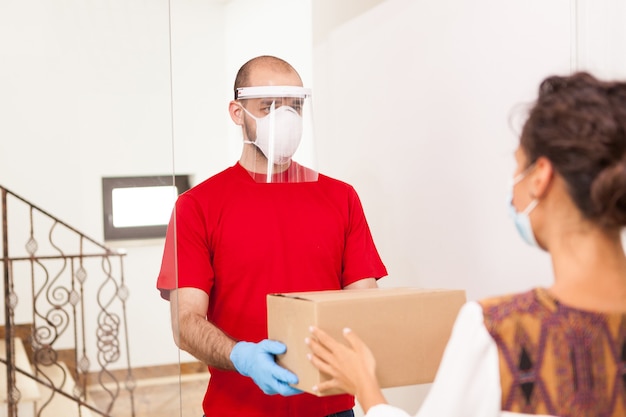 Delivery guy wearing protection mask holding box for customer.