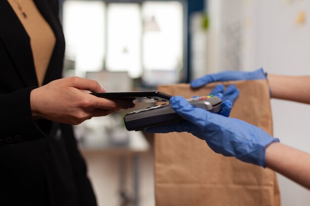 Delivery guy wearing protective gloves receiving paymant from businesswoman using smartphone nfc