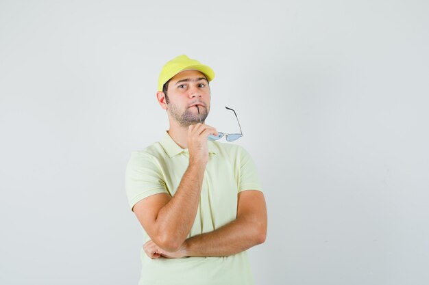 Delivery man biting glasses in yellow uniform and looking pensive , front view.