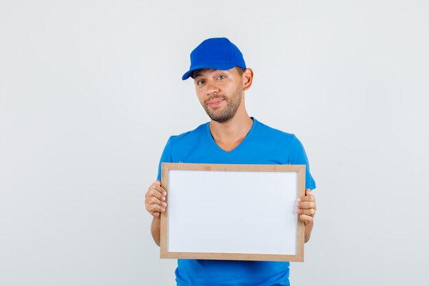 Delivery man in blue t-shirt, cap holding white board and looking cheerful