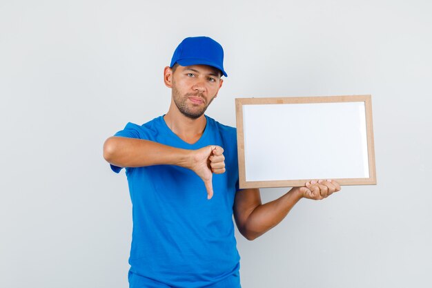 Доставщик в синей футболке, кепка держит белую доску большим пальцем вниз