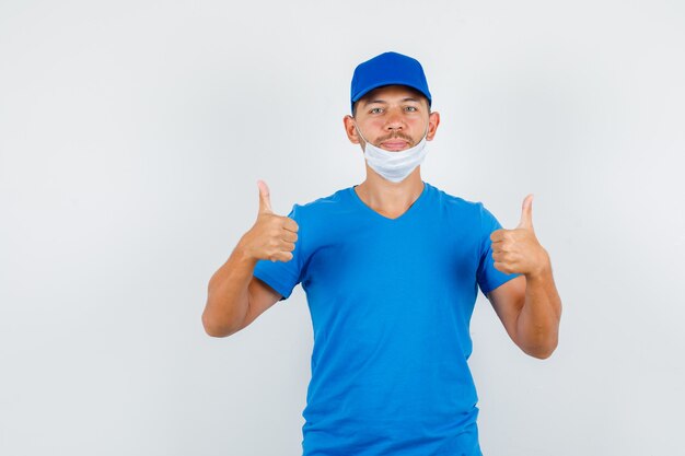 Delivery man in blue t-shirt, cap, mask showing thumbs up and looking positive