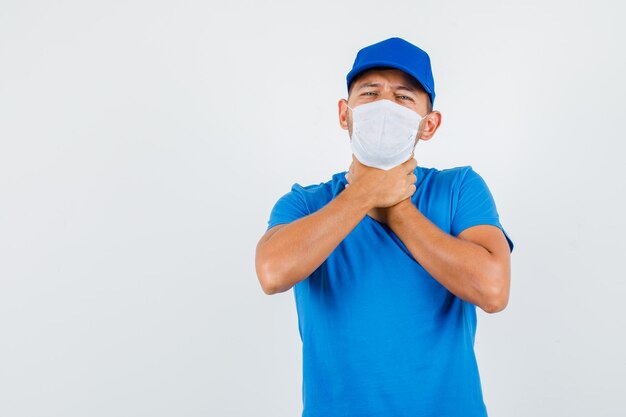 Delivery man in blue t-shirt, cap, mask suffering from a sore throat and looking sick