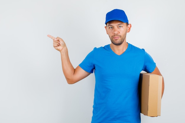 Доставщик в синей футболке, кепка указывает в сторону, держа картонную коробку