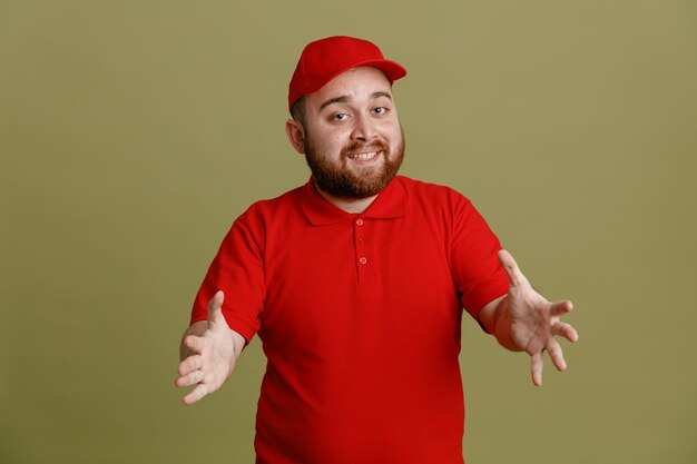 緑​の​背景​の​上に​立っている​何​か​を​保持している​ように​手​で​身振り​で​示す​赤い​帽子​の​空白​の​tシャツ​の​制服​を​着た​配達人​の​従業員
