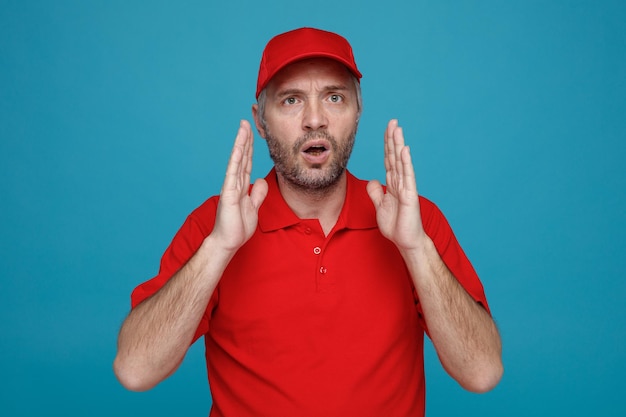 Free photo delivery man employee in red cap blank tshirt uniform looking at camera confused making size gesture with hands standing over blue background