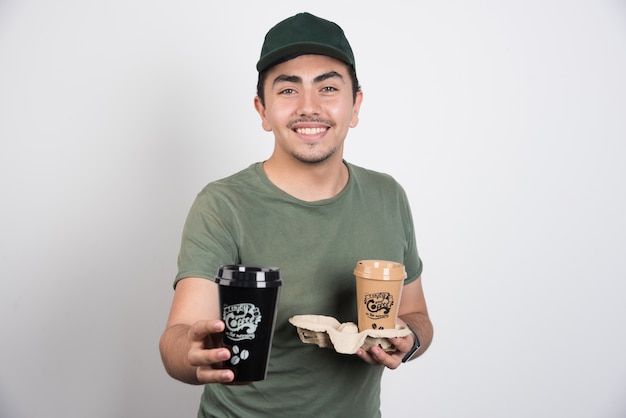 Delivery man giving away coffees on white background.