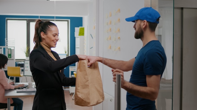 Delivery man giving takeaway package with food order to businesswoman working in startup business company office