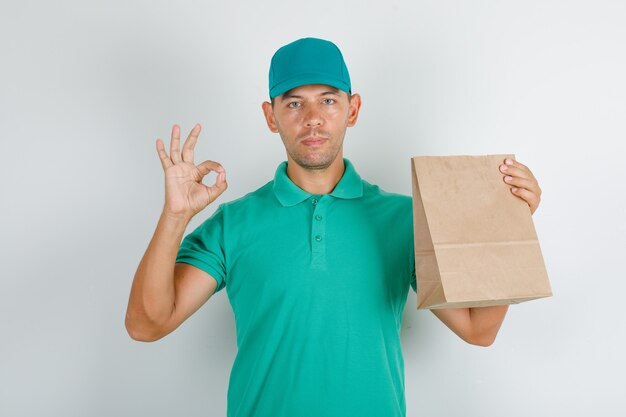 Delivery man in green t-shirt and cap doing ok sign with paper bag