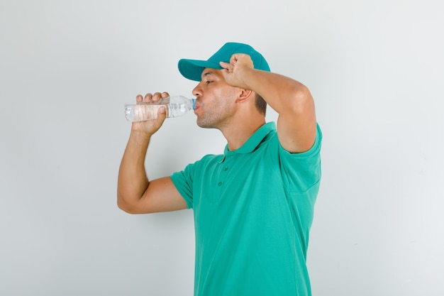 Free photo delivery man in green t-shirt and cap drinking water and looking thirsty
