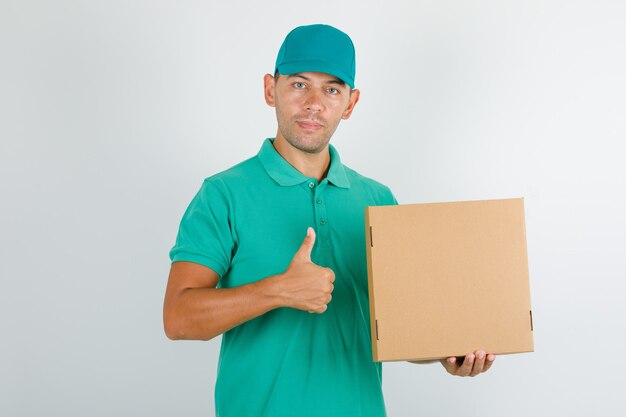 Delivery man in green t-shirt and cap holding box and showing thumb up