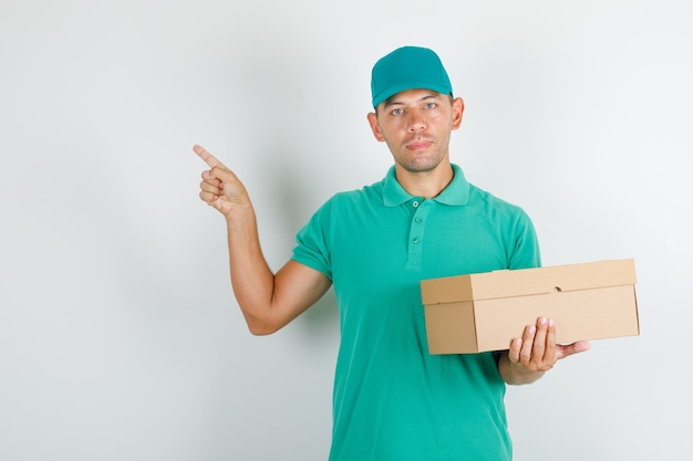 Доставщик в зеленой футболке и кепке, указывая что-то картонной коробкой